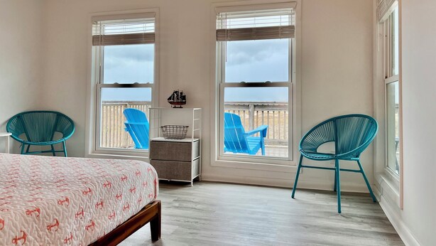 A bedroom with a bed, two windows, a balcony with chairs, and a small table. - Pet-Friendly Gulf Front Escape nestled in the Dunes (Dauphin Island)