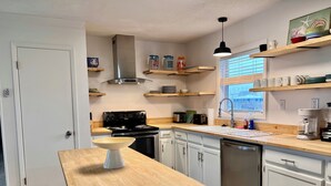 A modern kitchen with white cabinets, a wooden countertop, a stove, a sink, and a window with blinds. - Pet-Friendly Gulf Front Escape nestled in the Dunes (Dauphin Island)