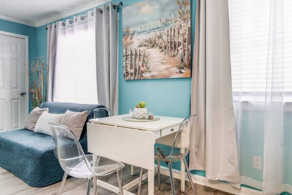 Een kamer met een blauwgroene wand, een wit bureau met een plant, een blauwe bank en transparante stoelen.