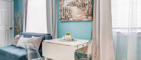 Een kamer met een blauwgroene wand, een wit bureau met een plant, een blauwe bank en transparante stoelen.