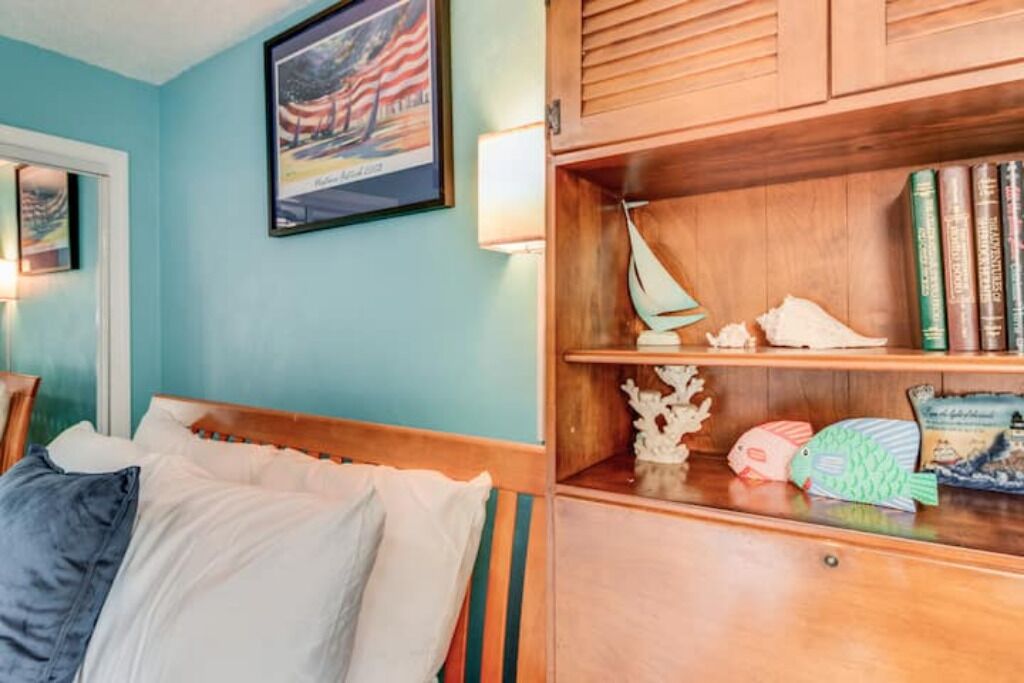 Een slaapkamer met een bed, een houten hoofdbord, een plank met decoratieve objecten en een ingelijste foto aan de muur.