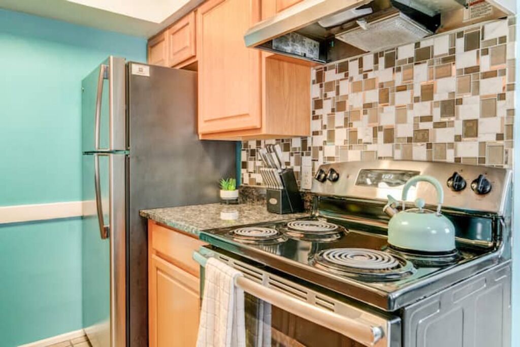 Una cocina con un refrigerador de acero inoxidable, estufa con un hervidor, armarios de madera y salpicadero de azulejos.