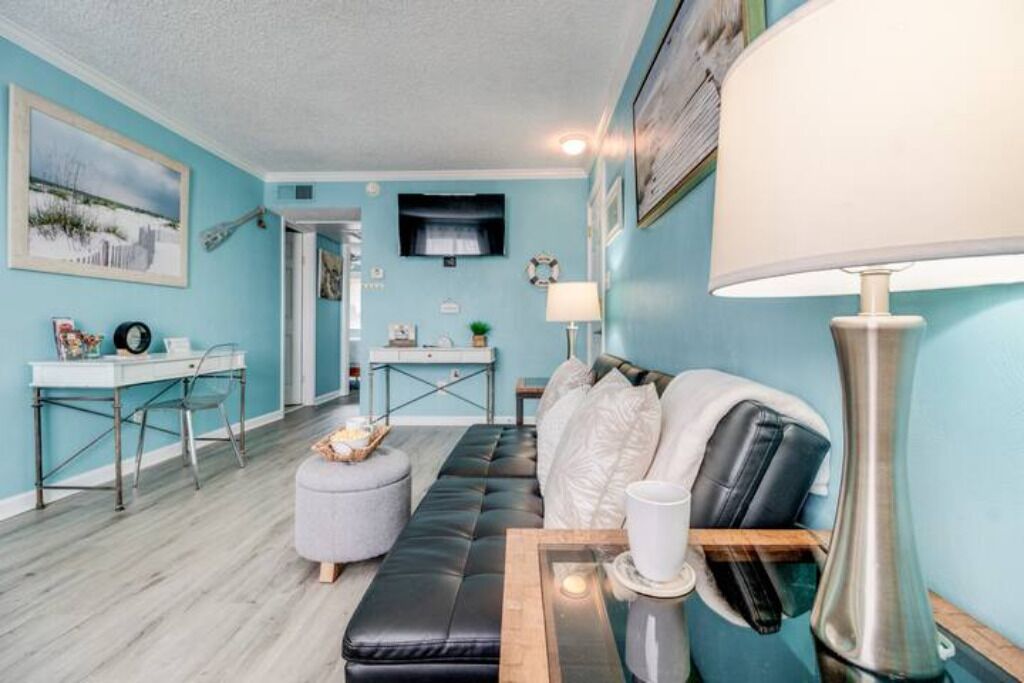 Un salon comprenant un canapé en cuir noir, une table basse blanche, un bureau avec une chaise et une lampe.