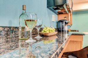 Una encimera de cocina con una botella de vino blanco, dos copas de vino y un bol de uvas verdes.