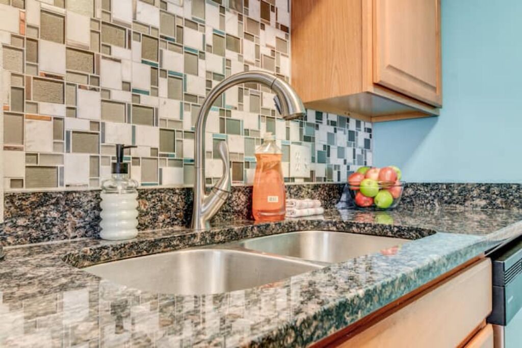 Una cucina con piano di lavoro in granito, lavello in acciaio inossidabile e schienale in mosaico.