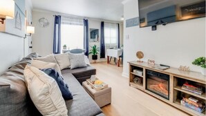 Ein modernes Wohnzimmer mit einem grauen Sofa, einem Kamin und einem an der Wand befestigten Fernseher.