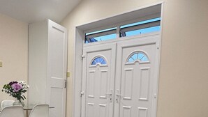 A room with a beige sofa, a dining table with chairs, and a set of double doors with windows. - Royal Modern Studio Heathrow London (Feltham)