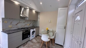 A compact kitchen with a gas stove, washing machine, and a glass dining table with chairs. - Royal Modern Studio Heathrow London (Feltham)