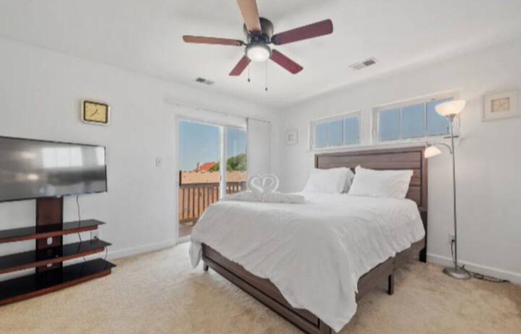A bedroom with a bed, a ceiling fan, a TV on a stand, and a window.