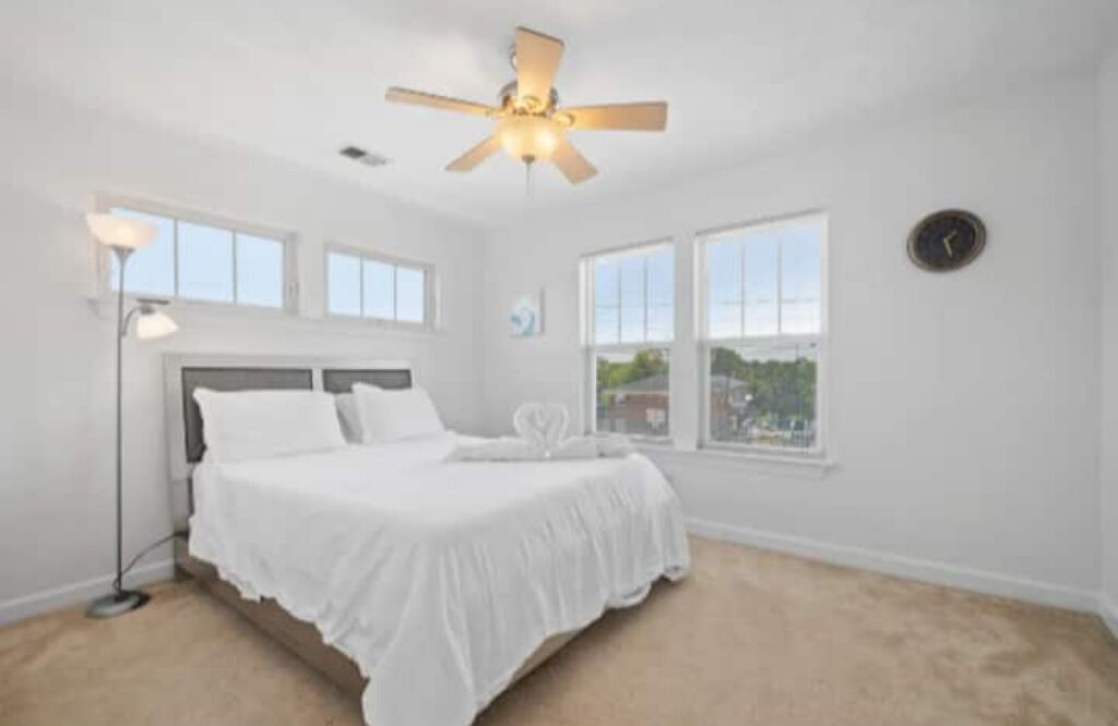 A bedroom with a bed, a ceiling fan, a window, and a clock on the wall.
