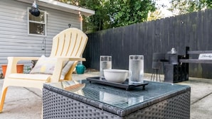 Un patio al aire libre con mobiliario de mimbre, una parrilla y una mesa de comedor.