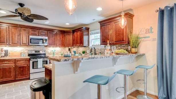 Una cocina moderna con armarios de madera, una isla central con taburetes de bar, microondas y ventilador de techo.