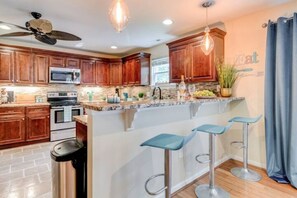 Una cocina moderna con armarios de madera, una isla central con taburetes de bar, microondas y ventilador de techo.