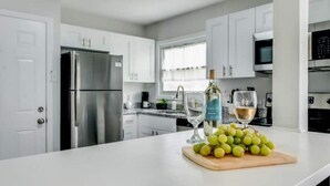 A modern kitchen with white cabinets, stainless steel appliances, and a countertop with a bottle of wine and a bunch of grapes.