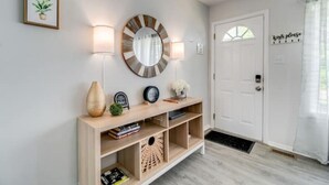 A hallway with a wooden console table, a round mirror, wall-mounted lamps, and a door with a 'keys please' sign.