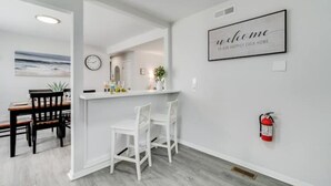 A modern kitchen with white cabinetry, a bar area with white stools, and a welcome sign on the wall.