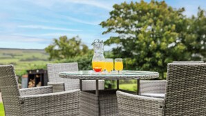 Un espacio exterior con sillas de mimbre y una mesa de vidrio, que incluye una jarra y vasos de jugo de naranja.