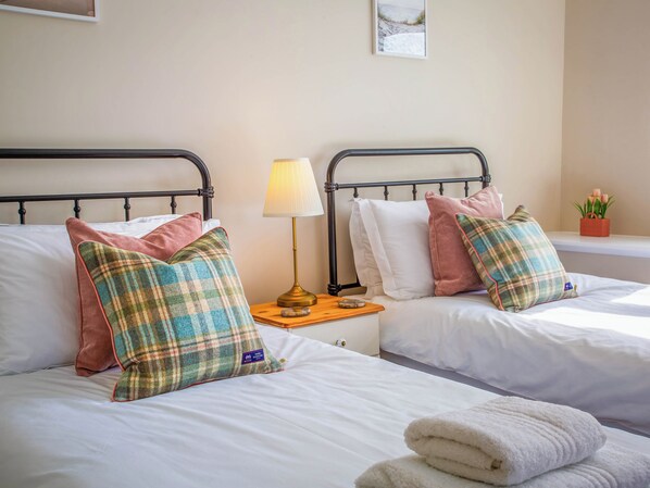 Dos camas individuales con ropa de cama blanca, una mesita de noche con lámpara y una pequeña planta en maceta.