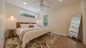 A bedroom with a bed, a ceiling fan, two windows, a large mirror, and a patterned rug. - Serene 2-bedroom apartment with WiFi in Ellsworth with a backyard stream. (Ellsworth)