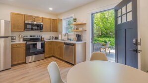 A modern kitchen with wooden cabinets, stainless steel appliances, and a dining area with a table and chairs. - Serene 2-bedroom apartment with WiFi in Ellsworth with a backyard stream. (Ellsworth)