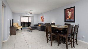 A spacious living room with a dining area, a ceiling fan, and a large window. - The 3 Queen Suite by 802 & Paredes (Brownsville)