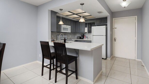 A modern kitchen with a central island, two pendant lights, and a white refrigerator. - The 3 Queen Suite by 802 & Paredes (Brownsville)