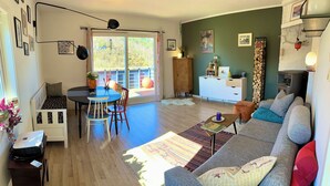 A living room with a sofa, a dining table with chairs, a cabinet, and a fireplace. - Cosy house with sunny balcony, mountains and fjord view! (Vestland)