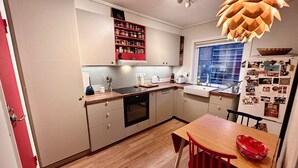 A modern kitchen with wooden cabinets, a built-in oven, and a red chair. - Cosy house with sunny balcony, mountains and fjord view! (Vestland)