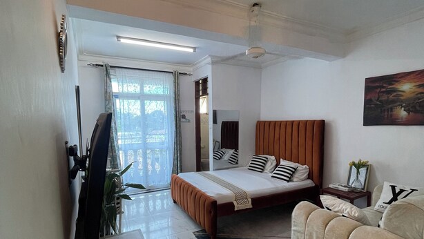 Une chambre moderne avec un lit, un canapé, une télévision et un bureau agrémenté d’une plante.