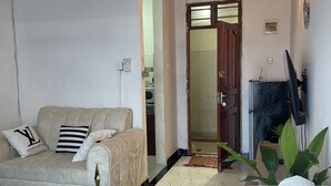 Un salon avec un canapé beige, un fauteuil marron, une télévision et une plante.