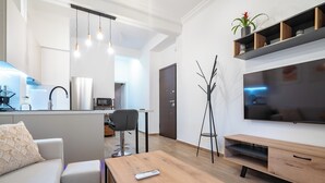 Uma sala de estar moderna com sofá, mesa de centro, TV e área de cozinha ao fundo.