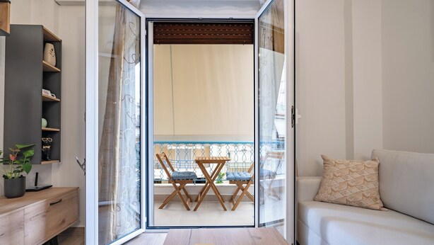 Uma sala de estar moderna com sofá, uma mesa de madeira e uma varanda com mesa e cadeiras.