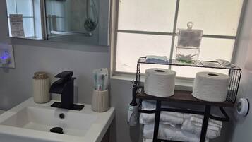A bathroom with a sink, mirror, towel rack, and a shower.