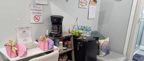 A compact living space with a TV, coffee maker, and a small fridge. There are signs for WiFi and no smoking.