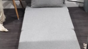 A single bed with a grey mattress and pillow in a room with a dark floor.