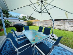 An outdoor patio with a table and chairs, a large umbrella, and a wooden fence in the background.