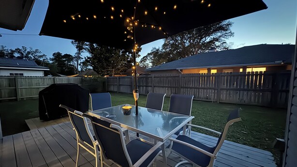 An outdoor patio with a glass table and chairs, string lights, and a barbecue grill. - Large home near the ocean, sleeps 1-11 guest! (Navarre)