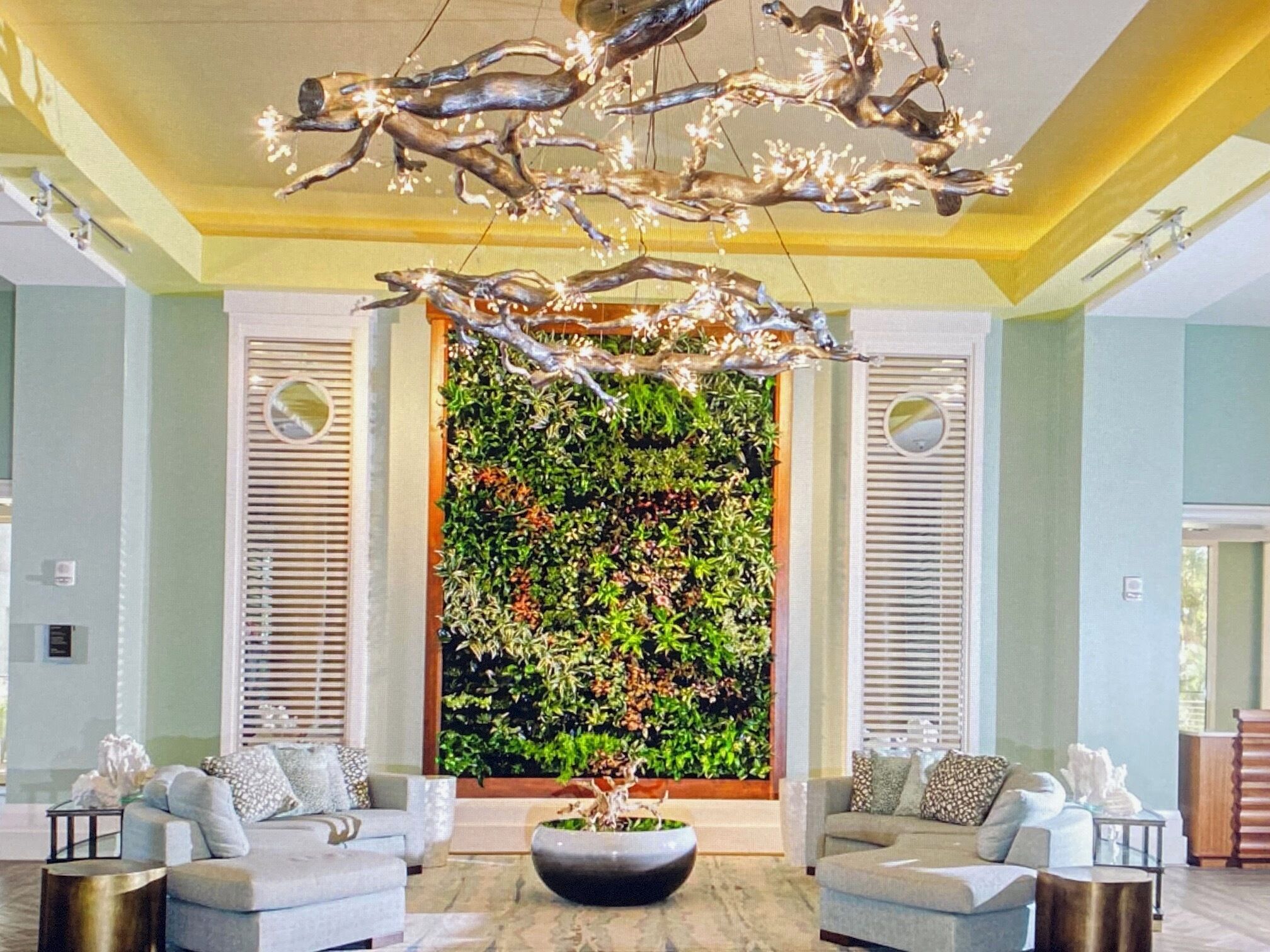 A modern lobby with two sofas, a large wall-mounted plant, and a unique chandelier.