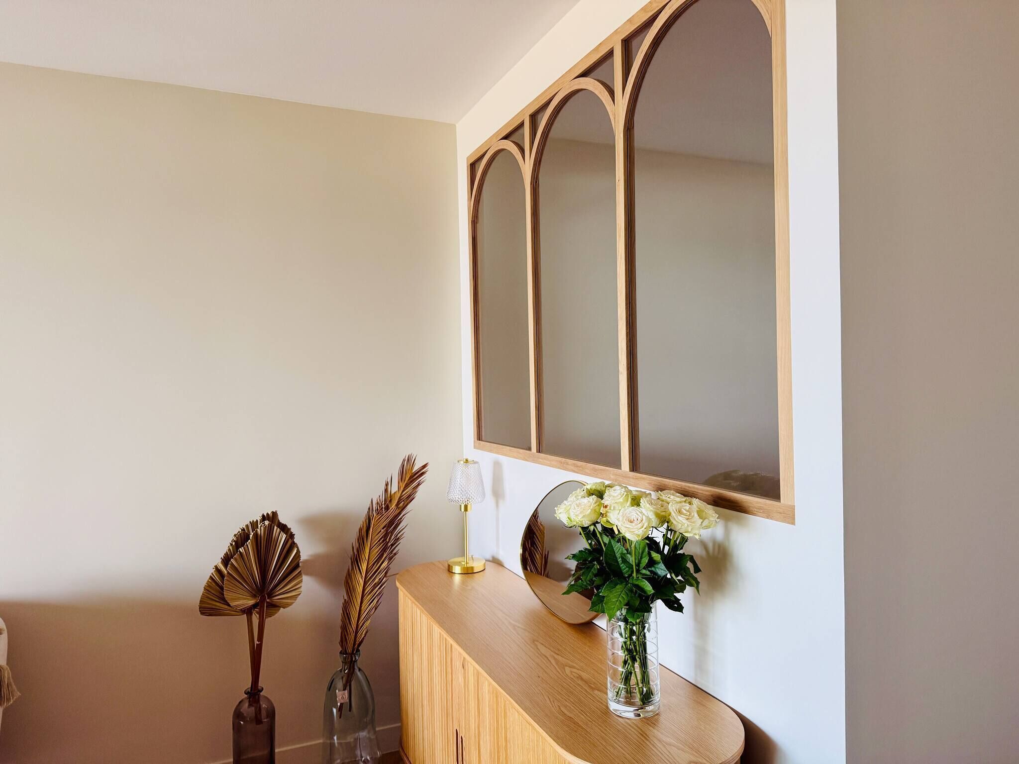 A wooden console table with a mirror, a vase of flowers, and decorative items.