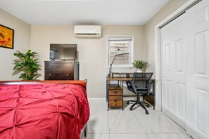 Ein Schlafzimmer mit Bett, Kommode, Schreibtisch, Stuhl und Klimaanlage.