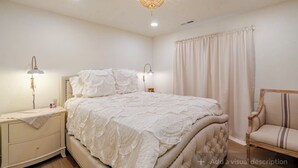 Une chambre à coucher avec un grand lit, deux lampes de chevet, une table de chevet, une chaise et une fenêtre avec des rideaux.