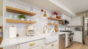 Une cuisine moderne avec des armoires blanches, des étagères en bois et des appareils électroménagers en acier inoxydable.