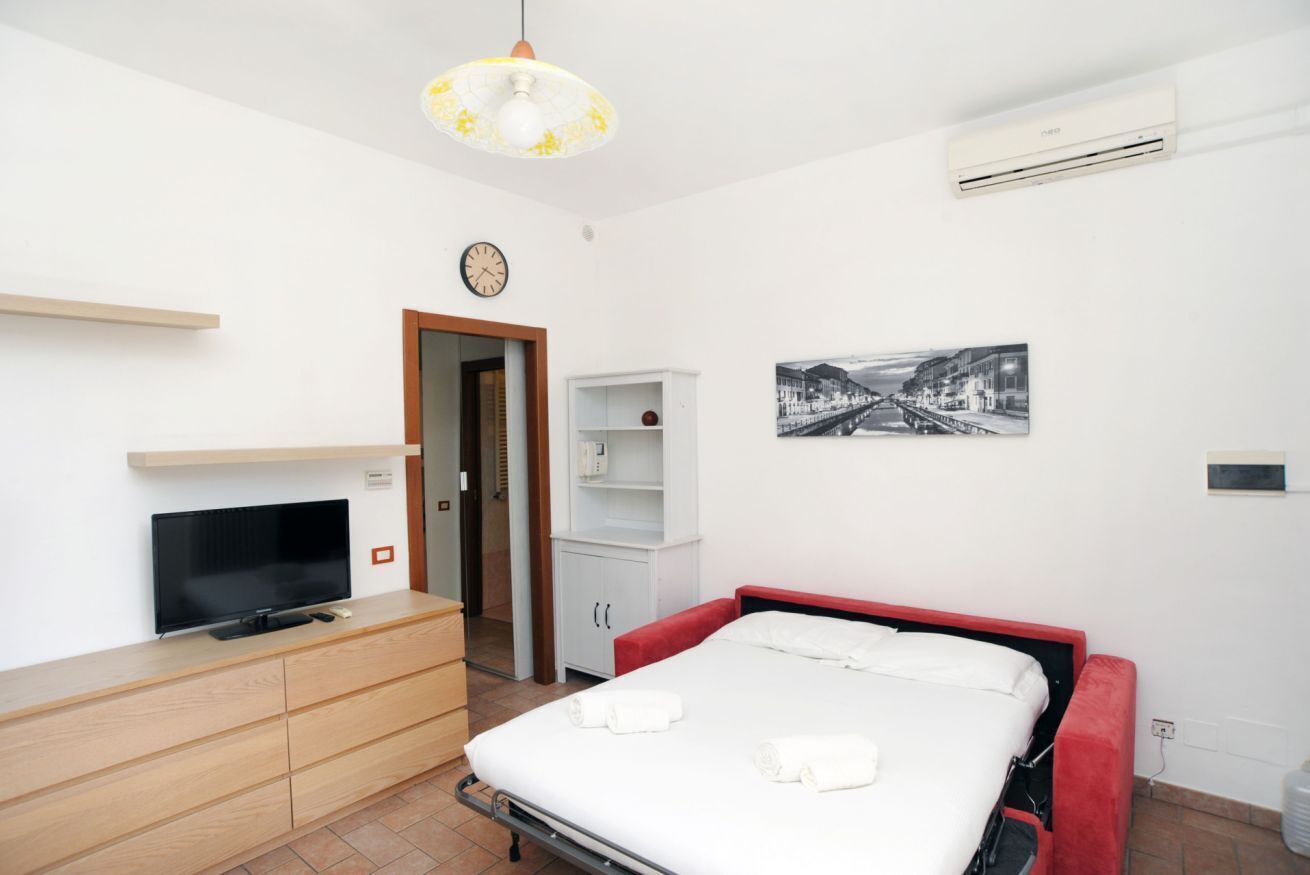 A hotel room with a bed, a TV, a wardrobe, a shelf, and a picture on the wall.
