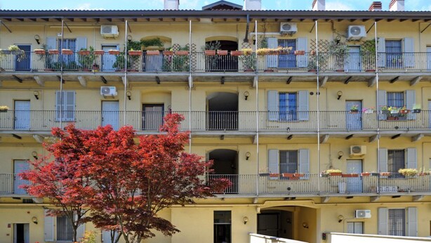 A multi-story building with balconies, air conditioning units, and a tree with red foliage in front. - Moro 137 Apartment Navigli  (MILANO)