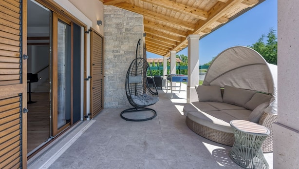 Un patio exterior con techo de madera, una silla colgante, una mesa redonda y un sofá.