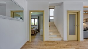 Un pasillo con piso de madera, una escalera y una puerta que da a otra habitación.