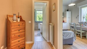 Un couloir mène à une chambre où se trouvent une commode en bois, un radiateur et un coin repas avec une table et des chaises.