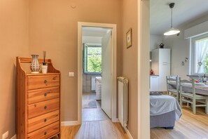 Un couloir mène à une chambre où se trouvent une commode en bois, un radiateur et un coin repas avec une table et des chaises.