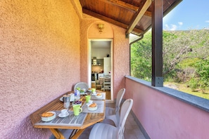 Un balcon avec une table dressée pour le petit-déjeuner, des chaises et une vue sur un jardin.