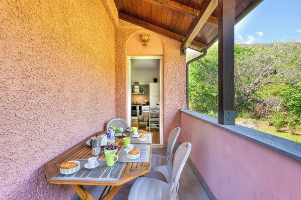 A wooden table set with breakfast items, a view of a garden, and a door leading to a kitchen.
